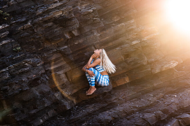 Frau sitzt mit Yogakleidung im Sonnenstrahl in einer Steinformation