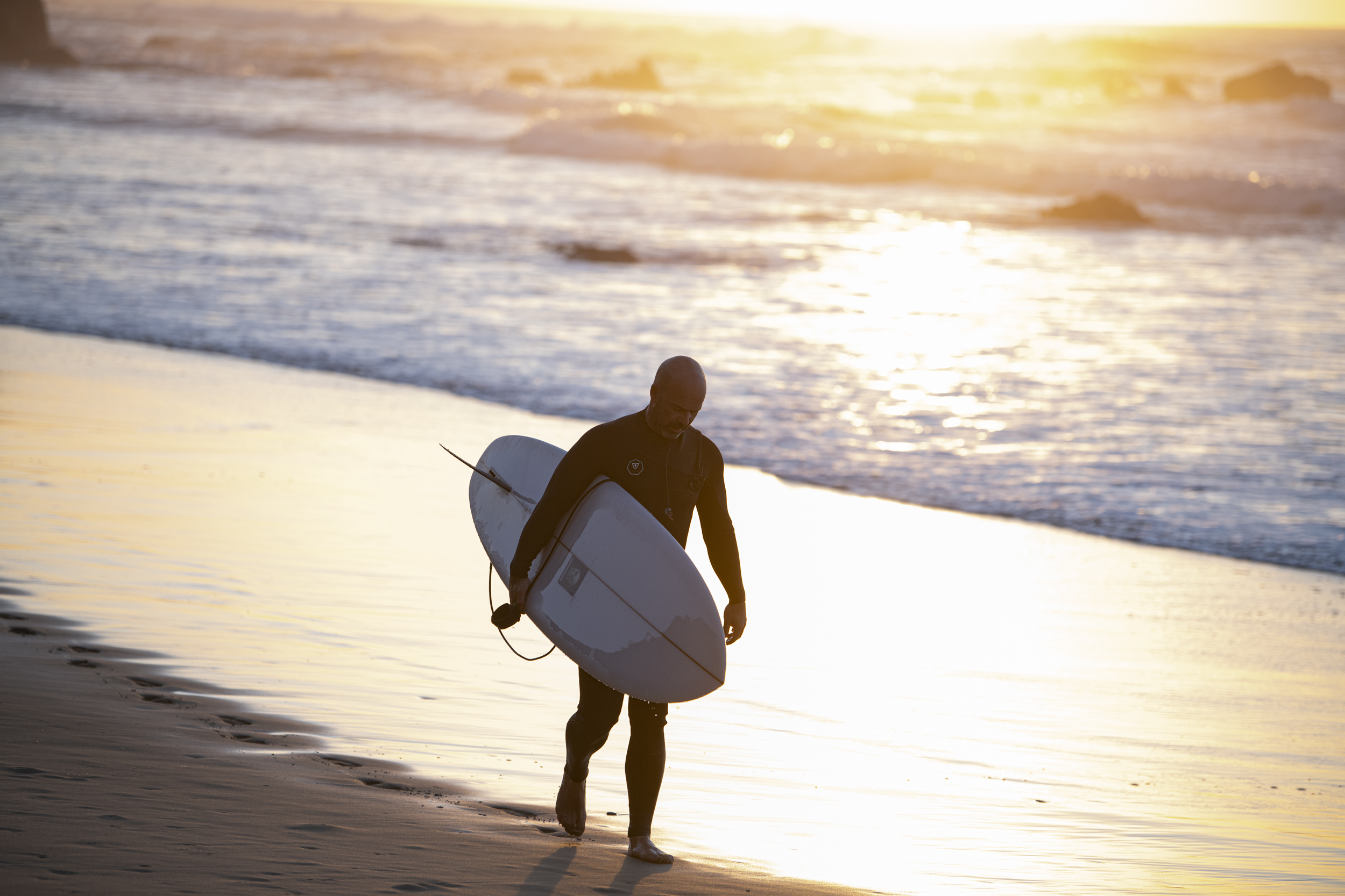 Mann trägt sein Surfbrett am Strand nach einer Surfsession.