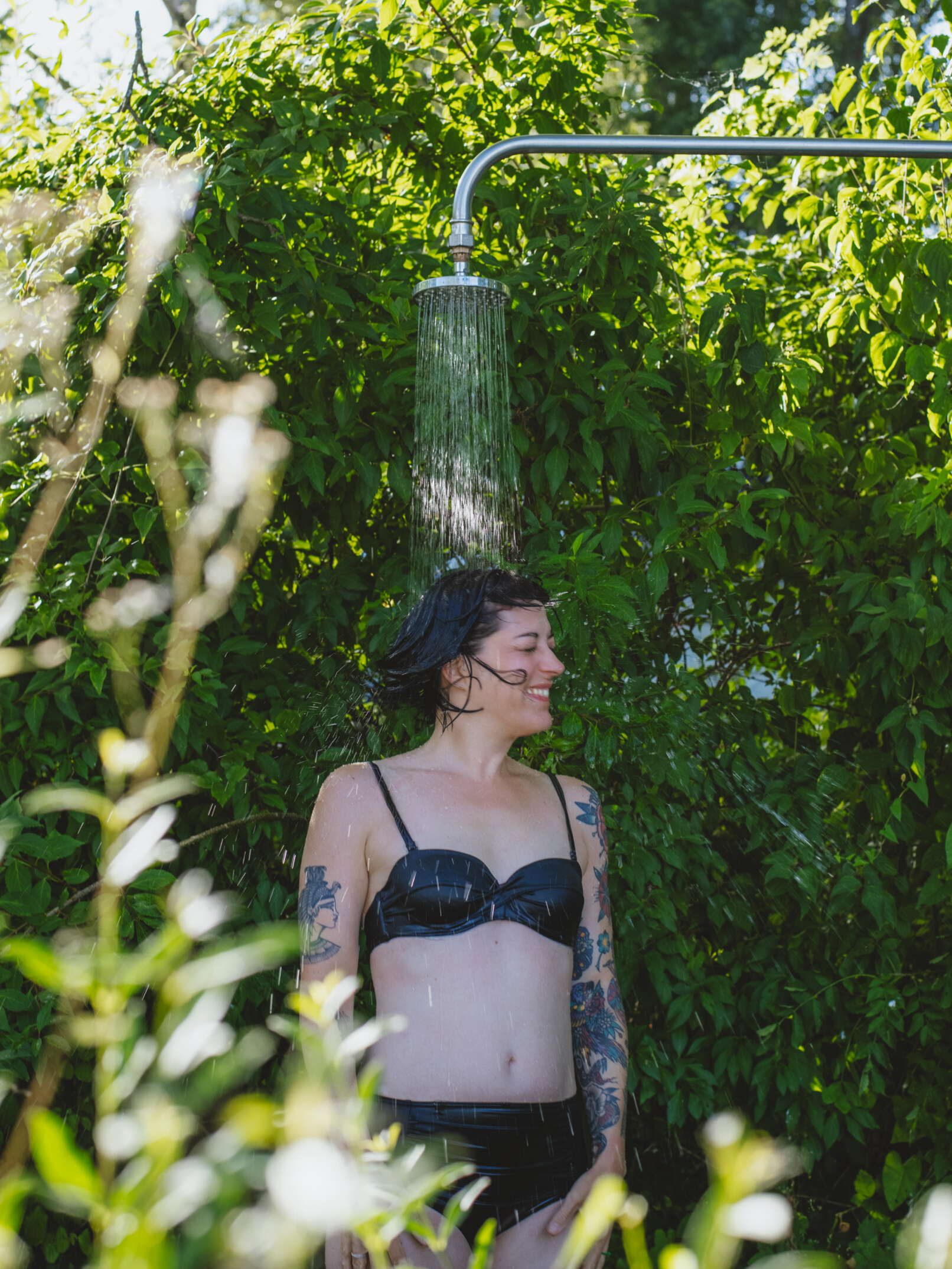 „Junge Frau unter einer Außendusche auf dem Naturcampingplatz am Bodensee, umgeben von sonniger, grüner Natur in sommerlicher Atmosphäre.“
